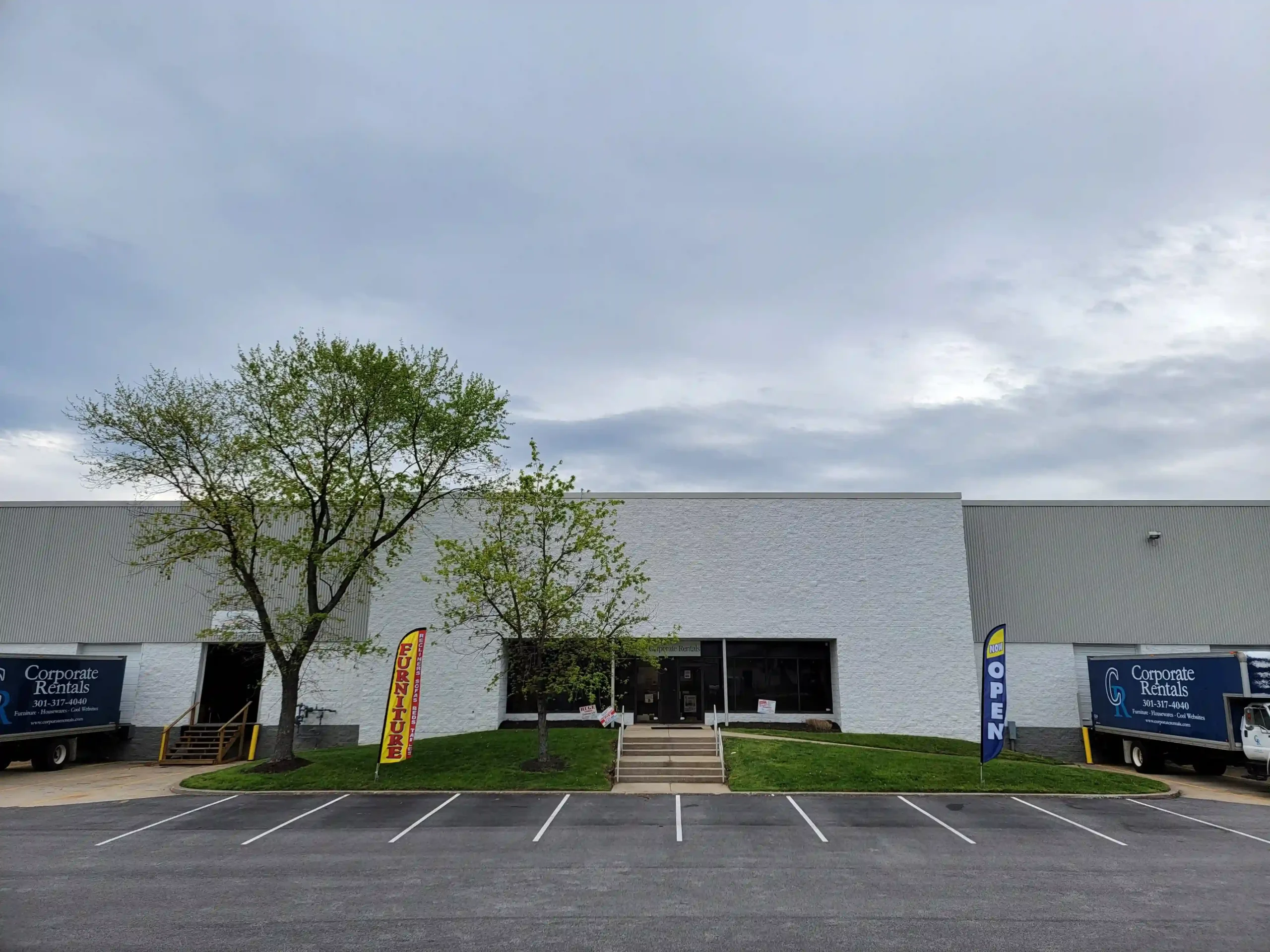 “Furniture Clearance Center entrance in Savage, MD with two flags and two corporate trucks outside.”