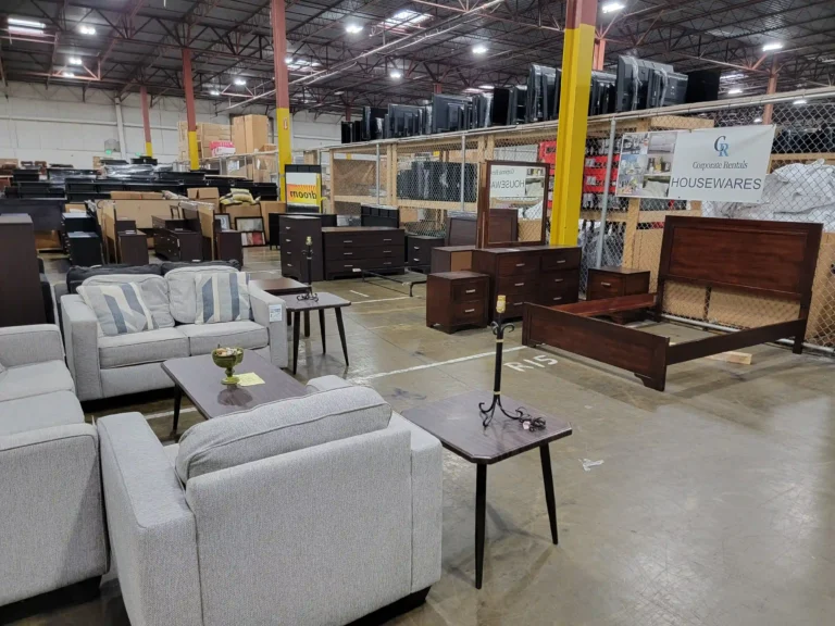 “Warehouse display of bedroom and living room furniture, showing sofas, chairs, coffee and end tables, and price tags for a clearance sale.”