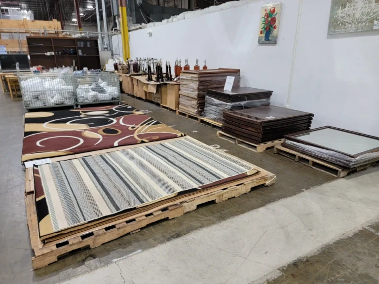 “Furniture clearance center warehouse display with rugs, mirrors, table lamps, sheets, and blankets.”