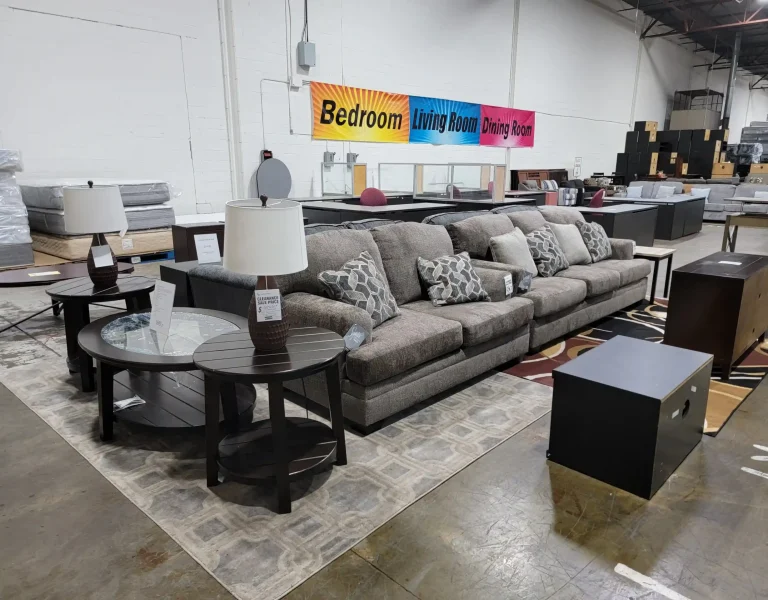 “Gray sofa and loveseat with throw pillows, coffee tables and TV stands on warehouse display, more furniture in the background.”